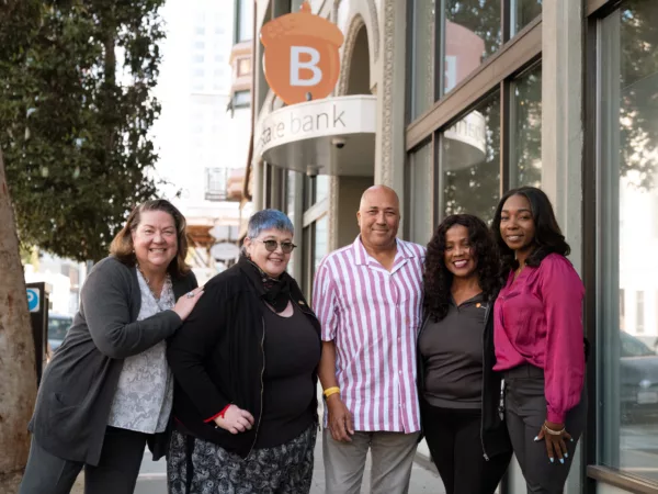 A group of Beneficial State Bank staff standing in front of the Oakland branch sign, smiling at the camera.