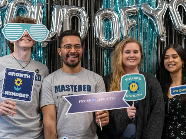 Four Doing Good Works team members pose at a company party with photobooth accessories with affirming statements.