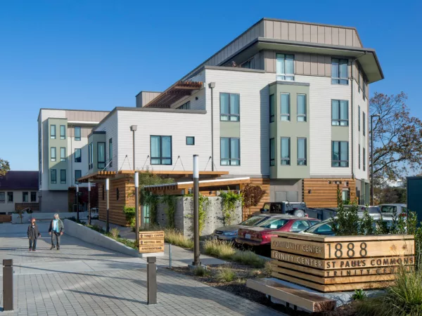 St. Paul's Commons Exterior. A modern looking white building with wood accents behind a parking lot and walkway.