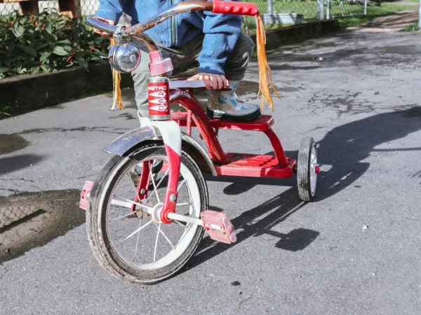 A child whose face we cannot see pushes a tricycle with streamers on the handle bars.